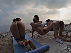 Three gorgeous girls doing naked yoga on rocky beach at sunset