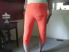 Male slut in skin-tight, bright orange spandex leggings.
