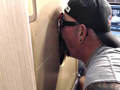 Gloryhole inked DILF sucks BFs cock through hole at home