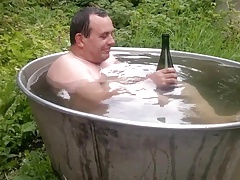 Naked old man rolls around in outside bath tub.